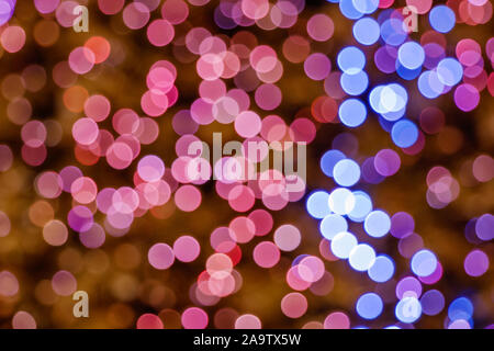 Illuminated Abstract round pink, purple, magenta, blue and gold bokeh on golden background. Colourful glitter bokeh from out of focus view of bulbs. Stock Photo