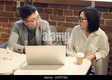 High angle portrait of two modern Asian business people discussing startup project while using laptop in office Stock Photo
