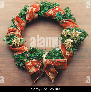 Christmas wreath isolated on wood background. Red ribbon on green artifical pine and red bow, golden flowers. Stock Photo
