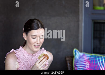 Young woman with smile on her face and eyes closed about to eat and enjoy a scone for morning tea