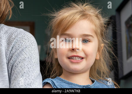 A close up portrait of a very cute little girl with big blue eyes and messy, fly away blonde hair.