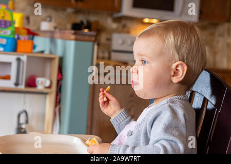 A very cute little girl sitting in her high chair having a snack. Stock Photo