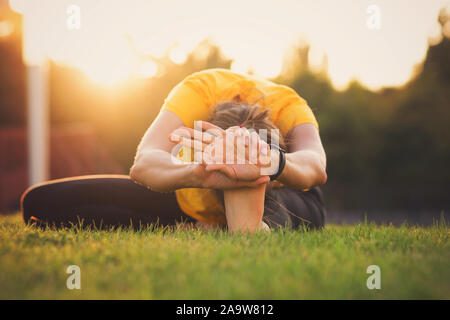 Young attractive woman practicing yoga in the park at sunset. Outdoor sport activity. Practice yoga asana. Healthy lifestyle. Pretty female sport girl Stock Photo