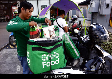 ANTIPOLO CITY, PHILIPPINES – NOVEMBER 16, 2019: Motorcycle delivery rider of a popular food delivery service company loads food for a customer to his Stock Photo