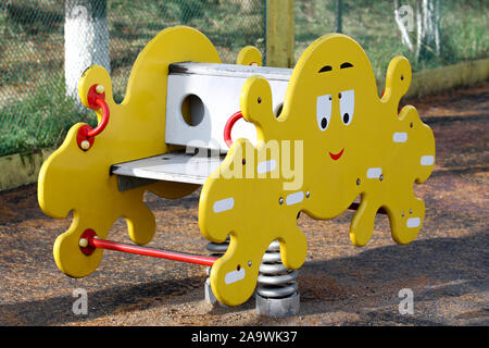 Spring swing with funny wooden octopus on kids playground. Yellow swing with benches for two toddlers. Amusing attraction for children Stock Photo