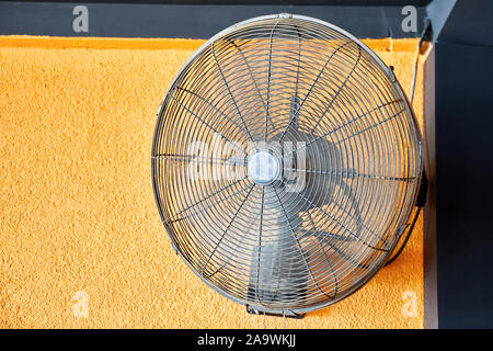 Vintage air cooling fan mounted on a yellow wall blowing air. Close up view. Stock Photo
