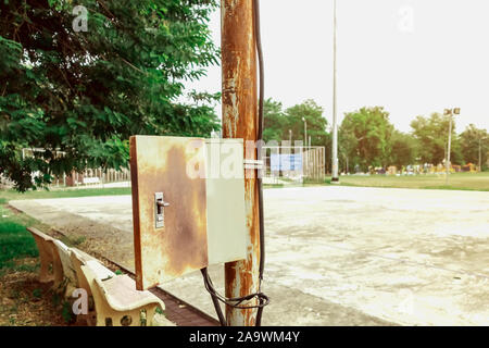 Old rusty electrical power control box on rusted electric pole in the public park. Stock Photo