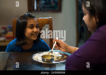 Young girl happily looks at her mother while she feeds her Stock Photo