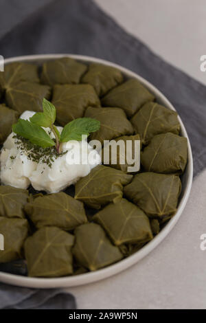 Staffed grape leaves (dolma) in a ceramic plate laying on light gray tabletop and dark gray linen napkin. Stock Photo
