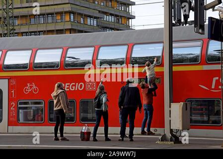 A child is given help to wave goodbye to someone in a double decker train at Aachen Station, Germany Stock Photo