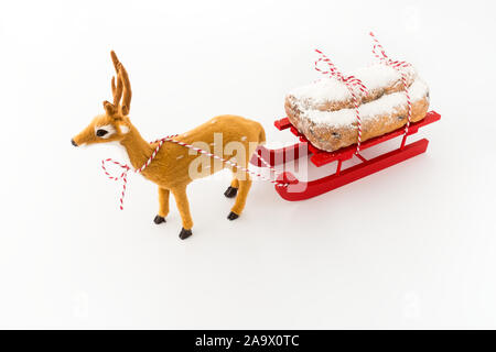 Deer pulling a red wooden sledge with stollen, a German Christstollen, isolated on white. Angled view. Stock Photo