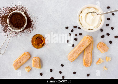 Tiramisu ingredients, ladyfingers, mascarpone, cocoa, almond liqueur and scattered black coffee beans on gray textured background with copy space. Top Stock Photo