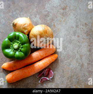 Flat lay of various vegetables including carrots, brown onions, garlic cloves and green pepper on a brown mottled background with white space Stock Photo
