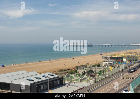 Brighton, England - August 24, 2019: View along beach and seafront promenade with Crazy Golf, Childrens playground and Palace pier. People walking. Stock Photo