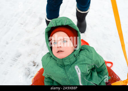 scared little boy rides on a sled in winter Stock Photo