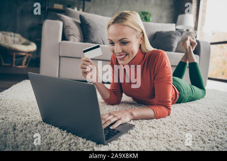 Photo of pretty homey lady choosing internet website notebook purchase prepared credit card for payment lying carpet floor near couch casual outfit Stock Photo
