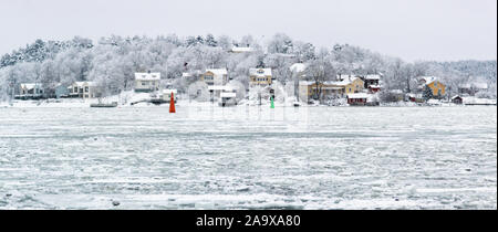 Snow covered traditional Finnish houses by the sea. Big cruise ships are passing through this narrow channel twice a day year-round, regardless of wea Stock Photo