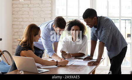Smiling mixed race colleagues explaining project ideas to female teammates. Stock Photo