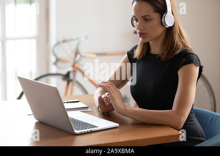 Concentrated businesswoman wearing wireless headphones, listening to educational seminar. Stock Photo