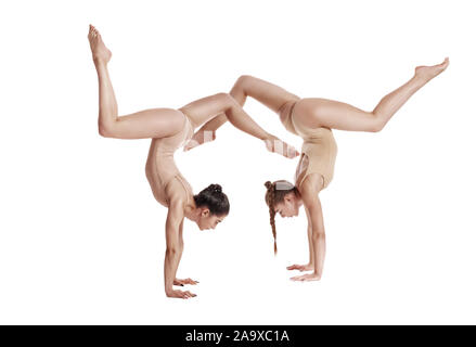 Two trained maidens gymnasts in beige leotards performing complex elements of gymnastics upside down, using support, posing isolated on white. Concept Stock Photo