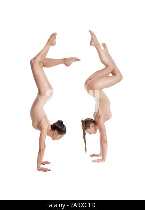 Two trained ladies gymnasts in beige leotards performing complex elements of gymnastics upside down, using support, posing isolated on white. Concept Stock Photo