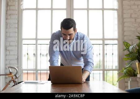 Young successful male manager leaning over table writing email. Stock Photo