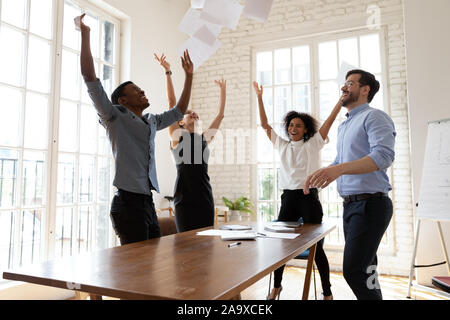 Overjoyed young multiracial team throwing papers in air. Stock Photo