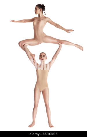 Two strong girls gymnasts in beige leotards performing complex elements of gymnastics using support, posing isolated on white. Concept of sports, fitn Stock Photo