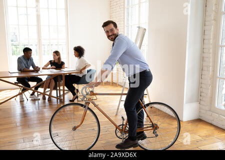 Playful happy young businessman riding bicycle at modern office. Stock Photo