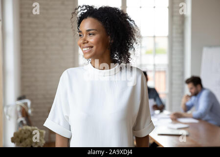 Happy dreamy african ethnicity young worker looking at window. Stock Photo