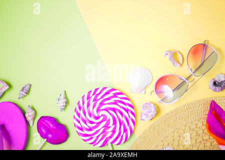 Beige straw beach sun hat, pink lollipops on pastel yellow and green background. Top view, close up. Beach accessories, summer, holiday. Stock Photo