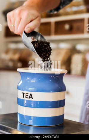 Close up of person standing in a kitchen, placing loose tea into striped blue ceramic jar. Stock Photo