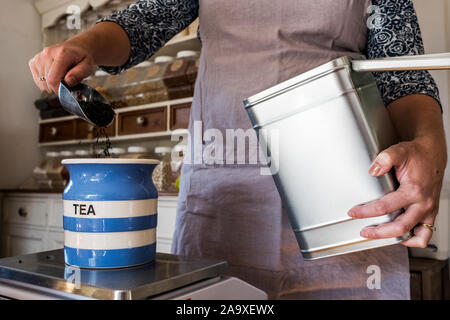 Close up of woman standing in a kitchen, placing loose tea into striped blue ceramic jar. Stock Photo