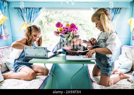 Two girls sitting at a table inside a blue caravan, playing. Stock Photo