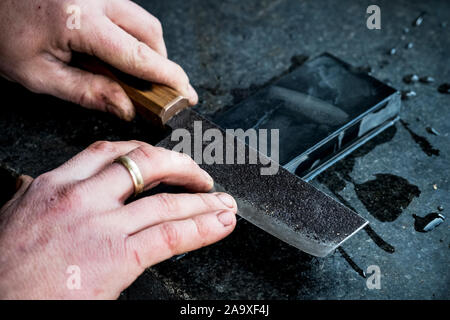 High angle close up of person sharpening handmade knife on a whetstone. Stock Photo