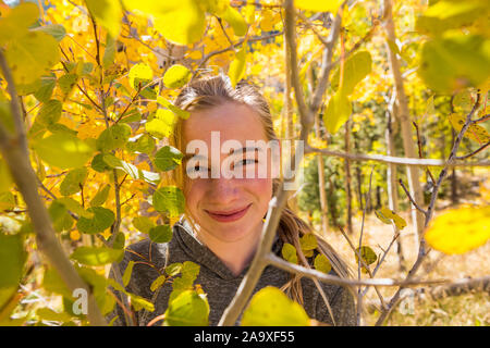 portrait of smiling 13 year old girl hiding behind autumn aspen leaves Stock Photo