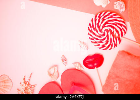 Bright flip flops with seashells and red lollipops in shape of lips on white and coral background. Flat lay composition. Beach, summer, holiday, sea, Stock Photo