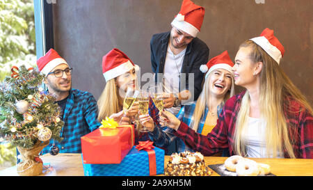 Happy young friends with santa hats celebrating Christmas toasting champagne at party. Stock Photo