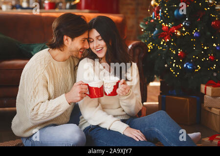 Couple in love having cocoa next to Christmas tree Stock Photo