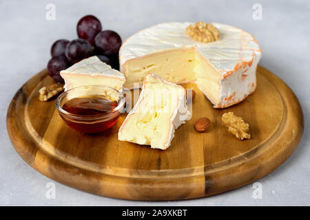 Close up of soft cheese on wooden tray with honey and grapes Stock Photo