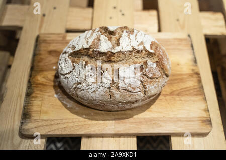 A fresh crusty rustic loaf of sourdough bread sat on a wooden bread board in the kitchen Stock Photo