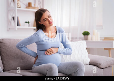 Pregnant Lady Having Massaging Lower Belly Sitting on Sofa Indoor