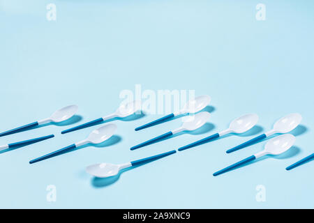 Beautiful and dangerous plastic spoons with blue handles on blue background. Flat lay, top view, copy space. Stock Photo