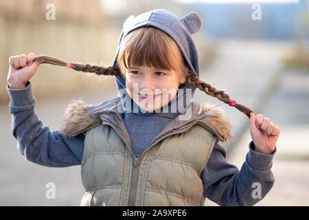 Portrait of happy child girl with hair braids in warm clothes in autumn outdoors. Stock Photo