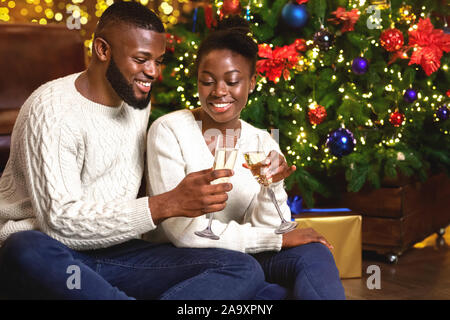 Happy afro couple holding and clinking champagne glasses, celebrating Christmas Stock Photo