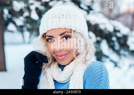 Smiling young woman touching face and looking at camera in winter park. Stock Photo