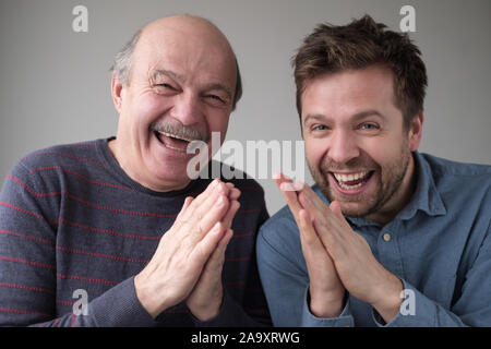 Tricky mature father and son smiling mysteriously, clasping hands, scheming something, keeping secret Stock Photo