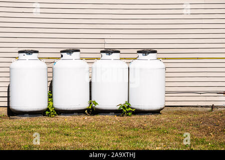 Row of white propane cylinders along the back wall of a house Stock Photo