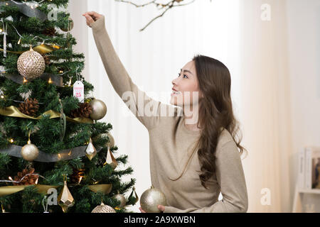 Asian woman hanging gold Christmas ball on Christmas tree Stock Photo
