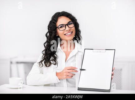 Smiling latin woman showing blank clipboard at office Stock Photo